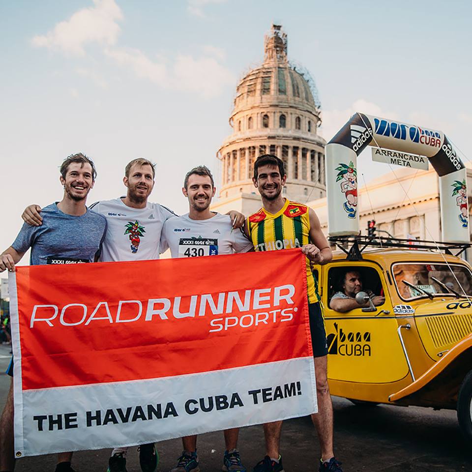 Four runners stand with an orange and white custom flag in front of them. 